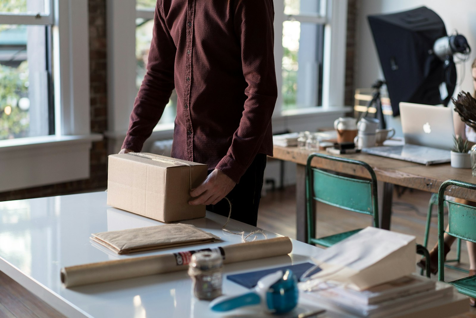 A small business owner packing a cardboard box for an online order at a home office desk